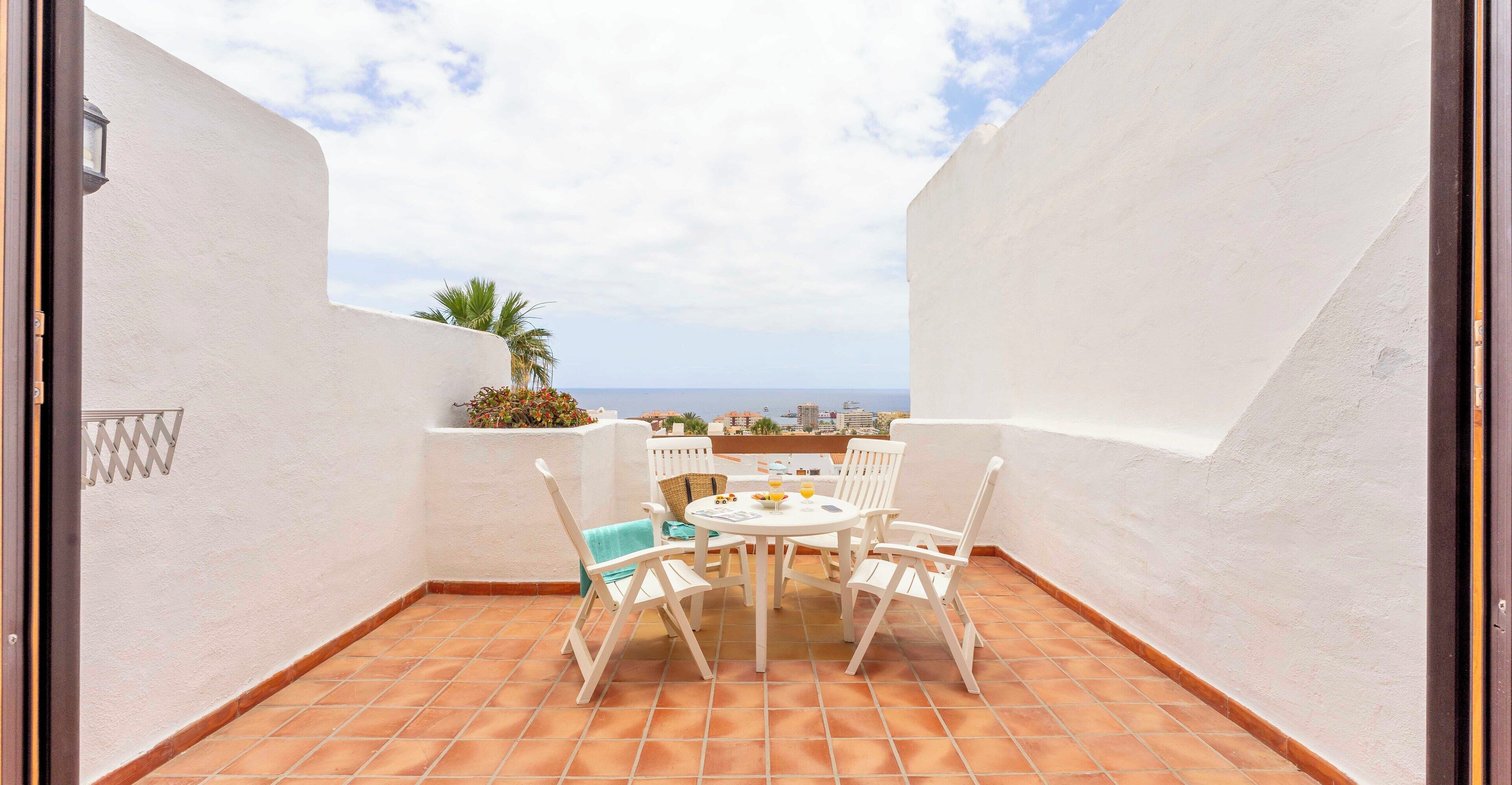 Een terras met een witte tafel en stoelen, een uitzicht op zee en een witte muur.