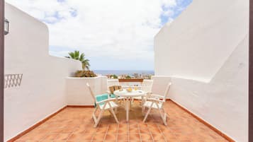 Una terraza con una mesa y sillas blancas, vista al mar y una pared blanca.