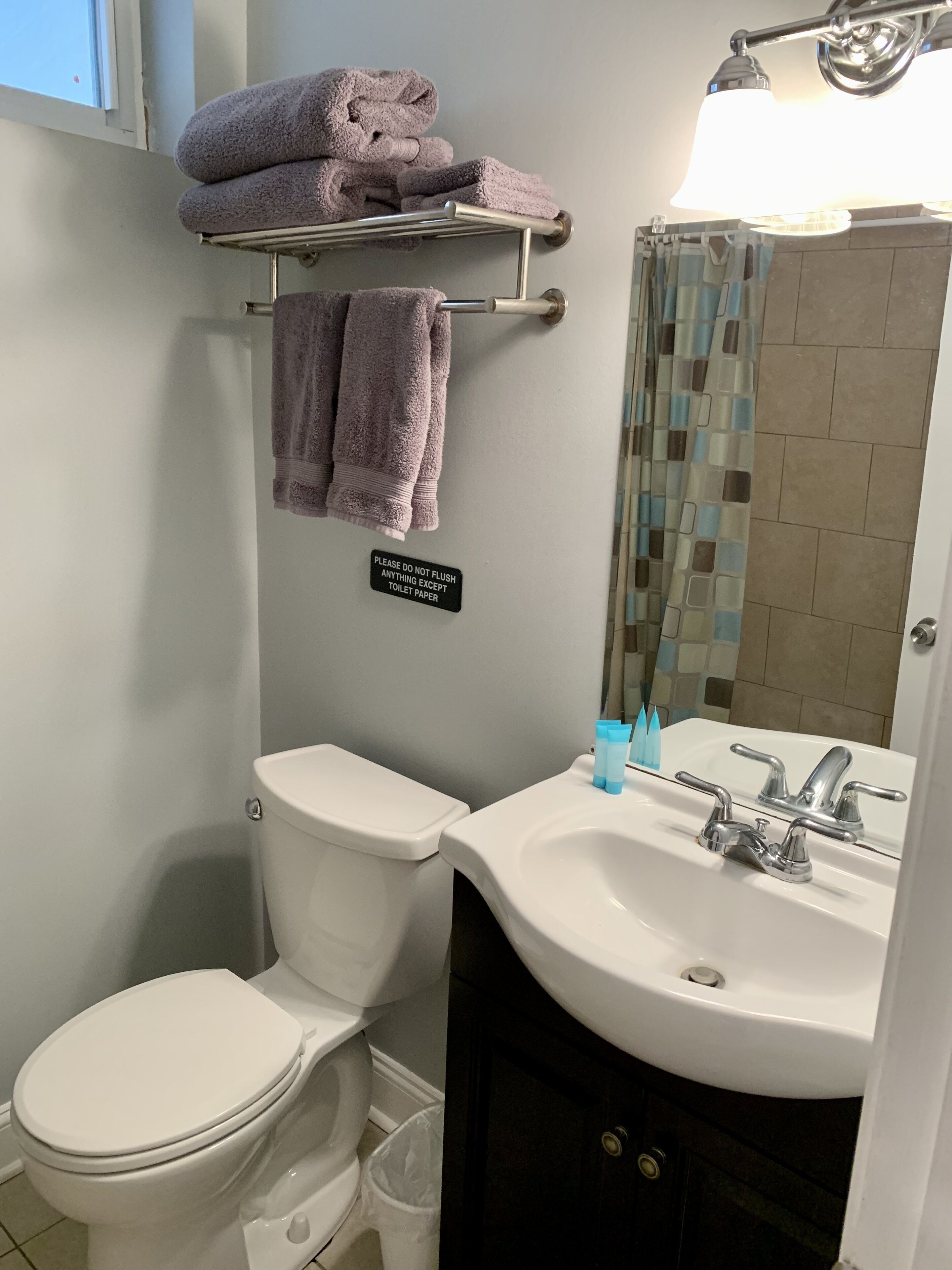 A bathroom with a toilet, sink, and a towel rack with folded towels. A sign on the wall reads "PLEASE DO NOT FLUSH ANYTHING EXCEPT TOILET PAPER."
