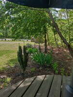 Una terraza de madera con vistas a un jardín ajardinado, que incluye varias plantas y una valla de madera al fondo.