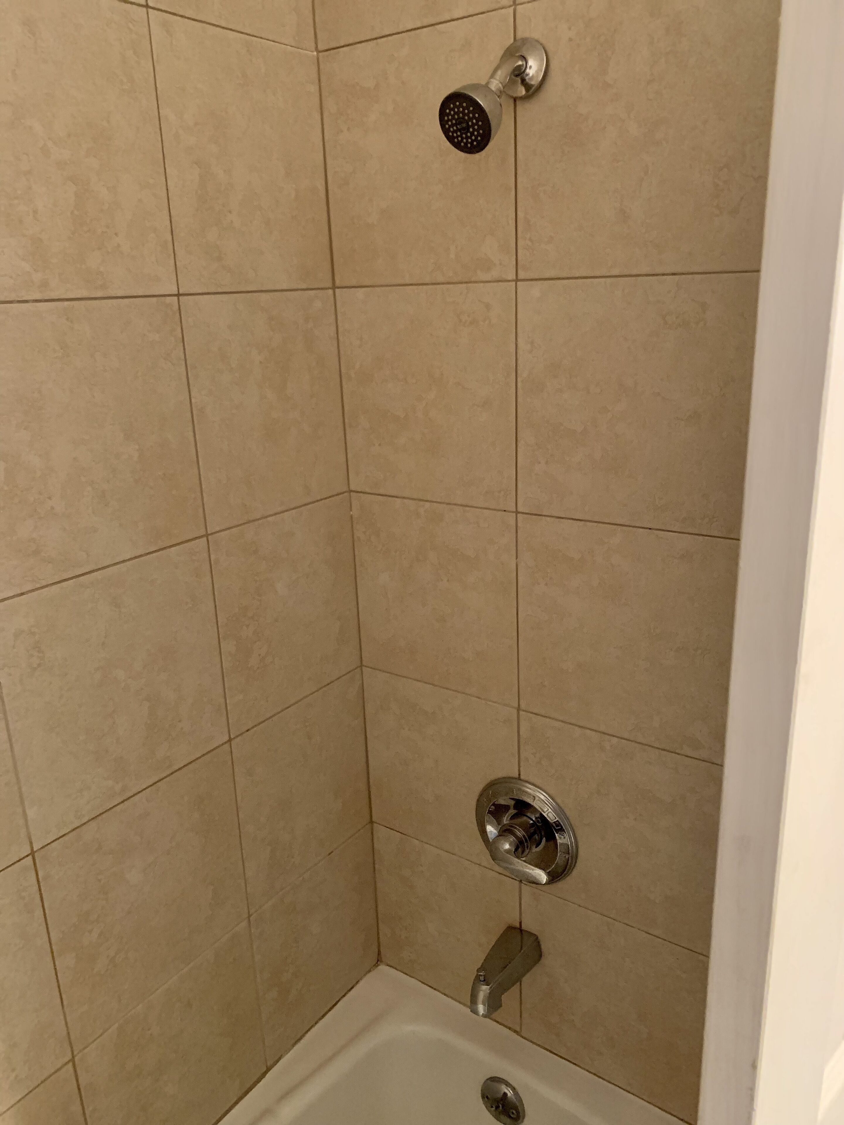 A shower area with beige tiles, a handheld showerhead, and a wall-mounted faucet.