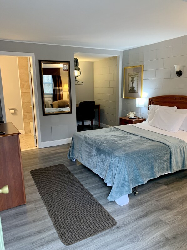Habitación de hotel con cama, escritorio, silla, espejo, lámpara y mesita de noche.