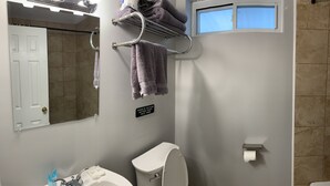 Baño con inodoro, lavamanos y toallero. Un cartel en la pared indica que solo se puede tirar papel higiénico.