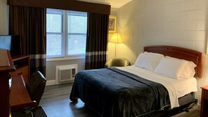 Habitación de hotel con cama, escritorio, silla, lámpara y ventana con cortinas.