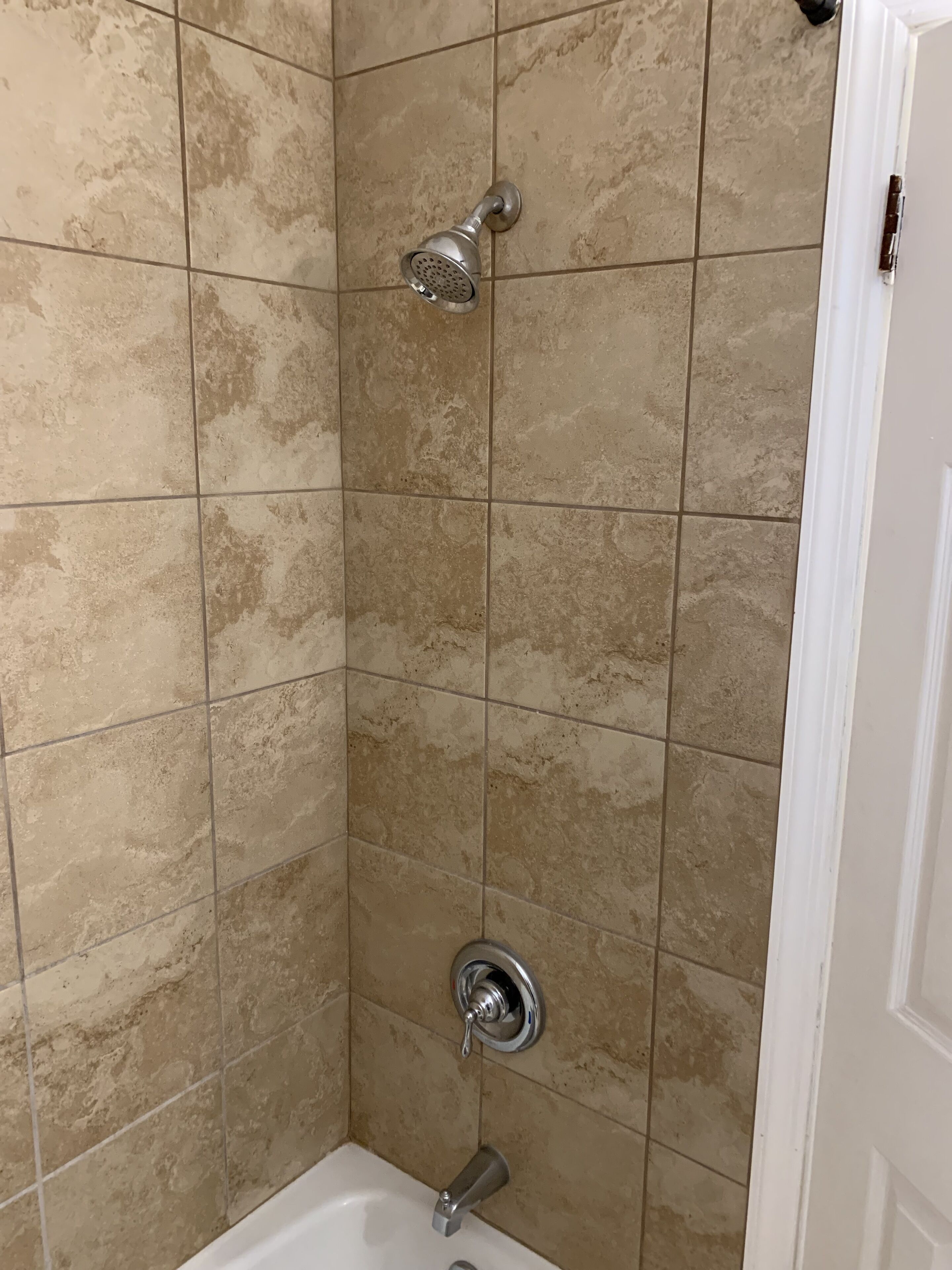 A corner shower with beige tiles, a handheld showerhead, and a wall-mounted faucet.