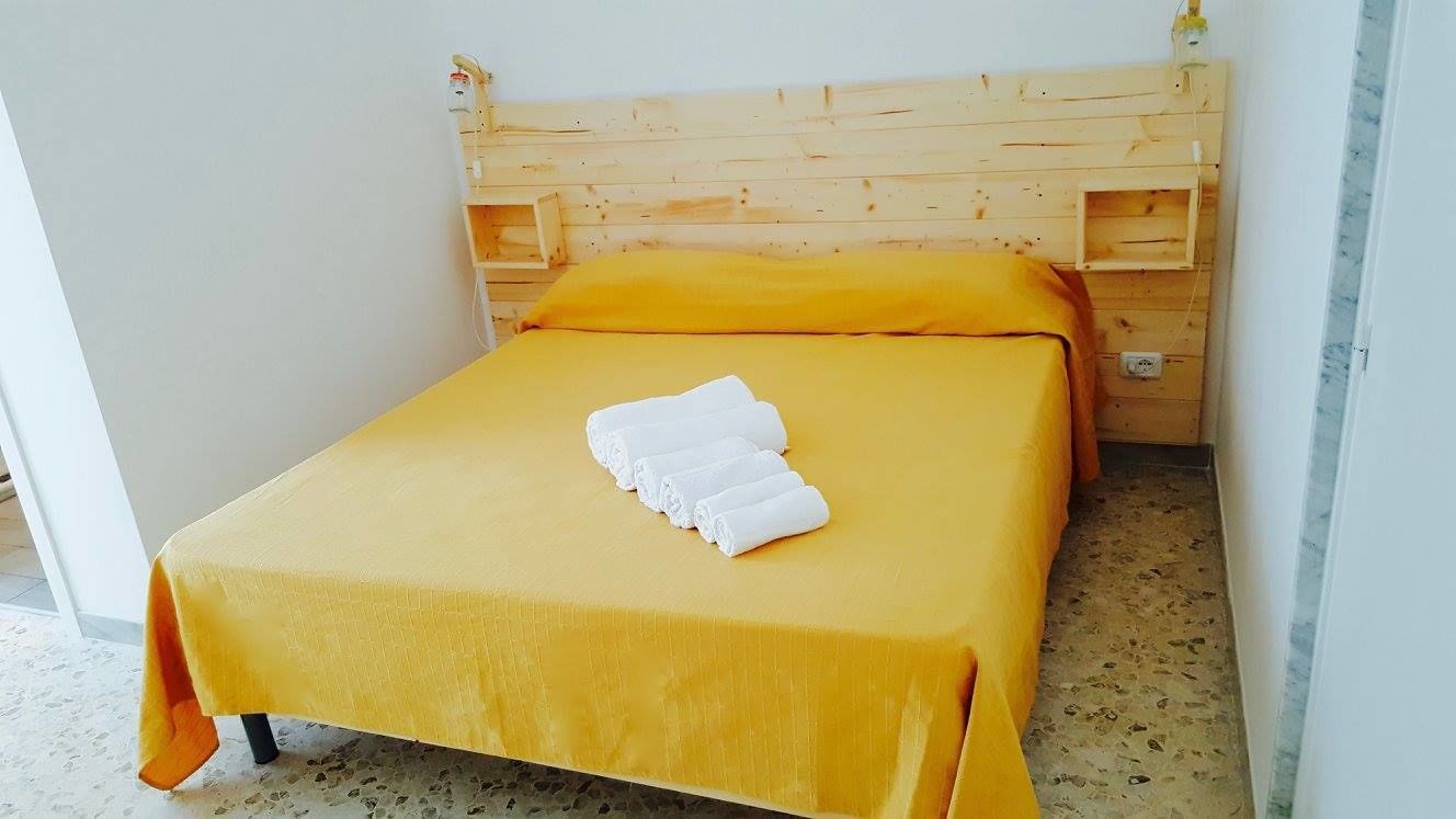 A single bed with a wooden headboard, a yellow bedspread, and a white towel folded on the bed.