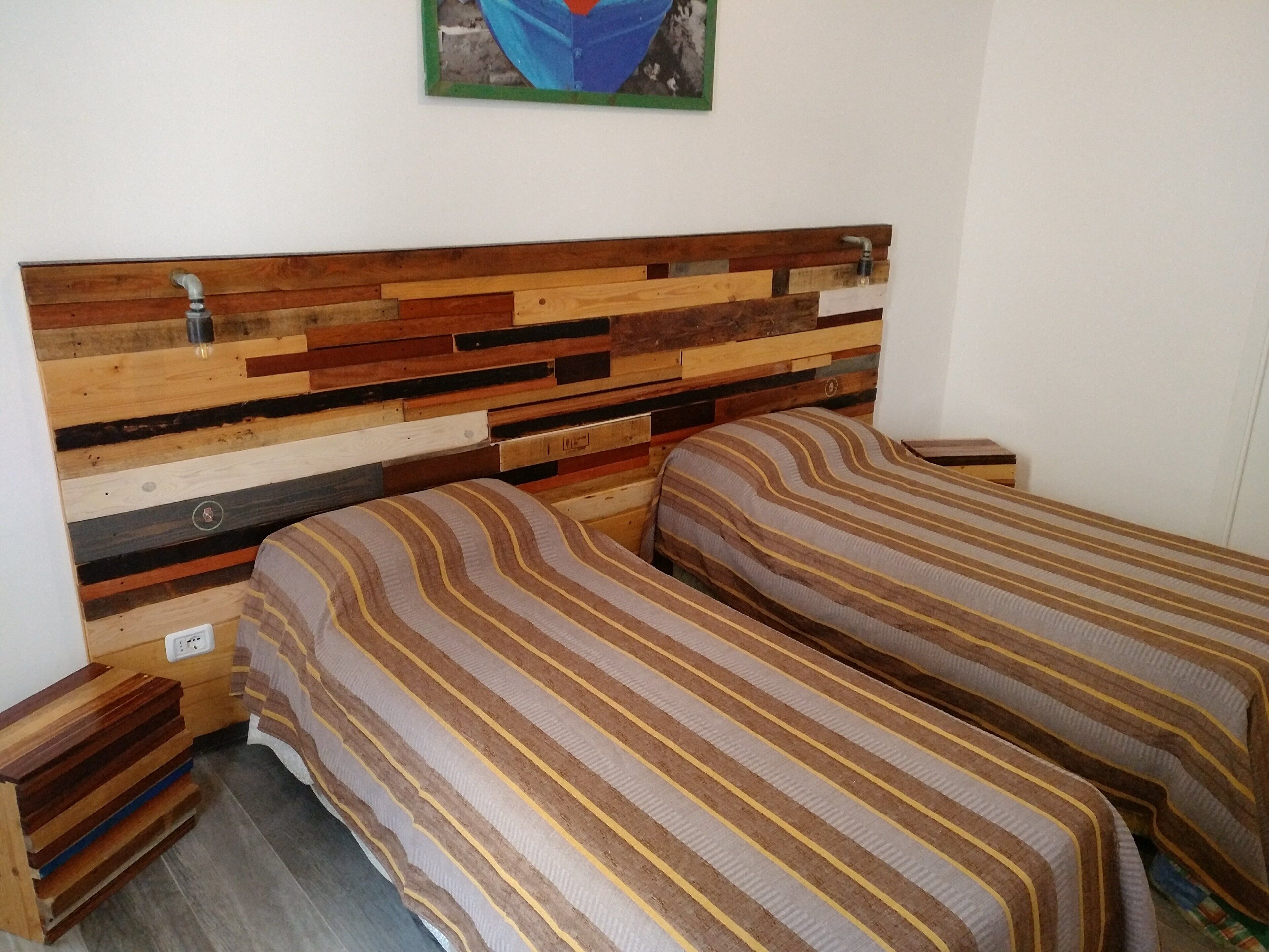 A bedroom with a wooden headboard, two beds with striped bedding, a nightstand, and a wall-mounted painting.
