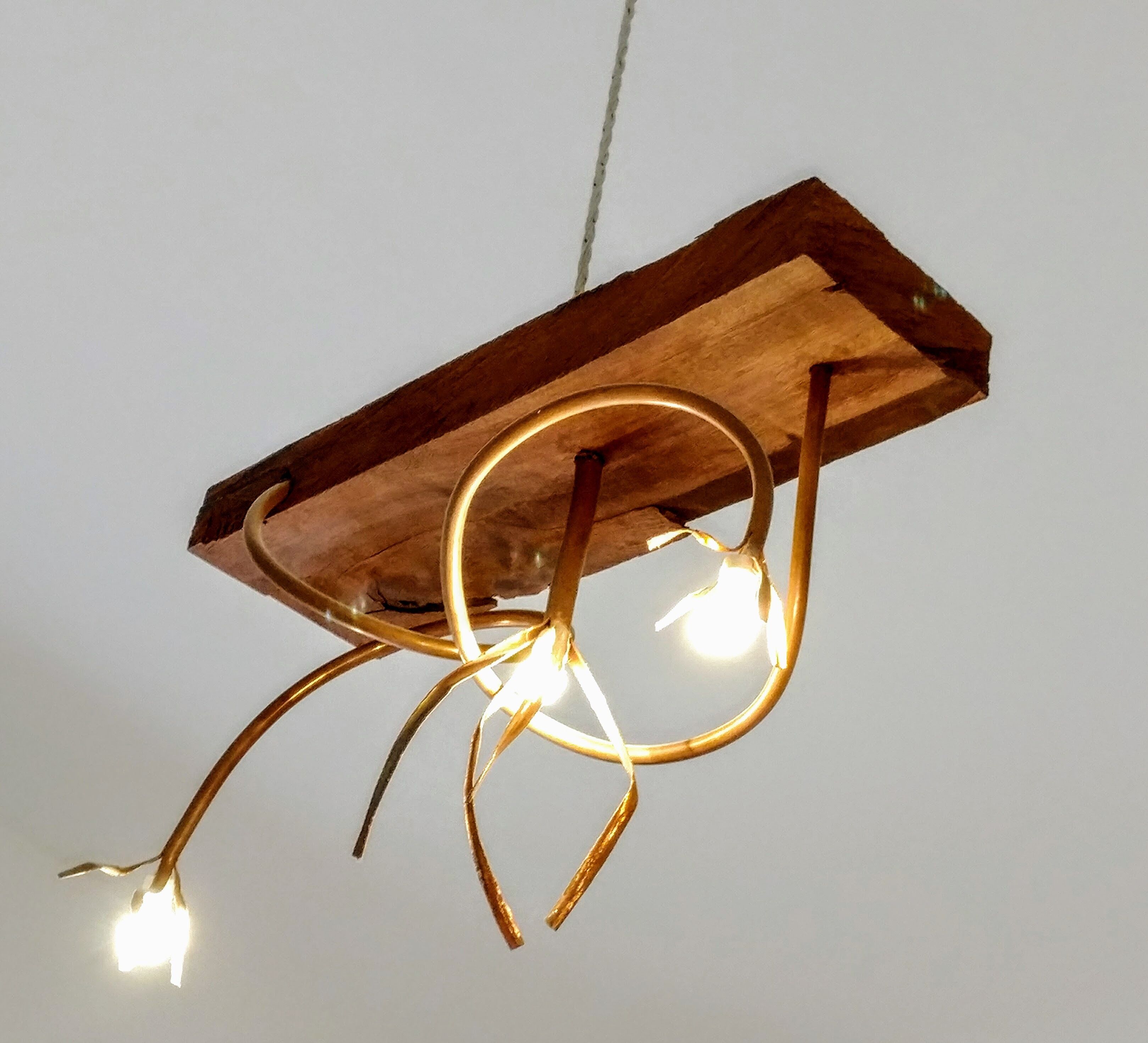 Eine Pendelleuchte mit Holzfuß und gebogenen Metallarmen.