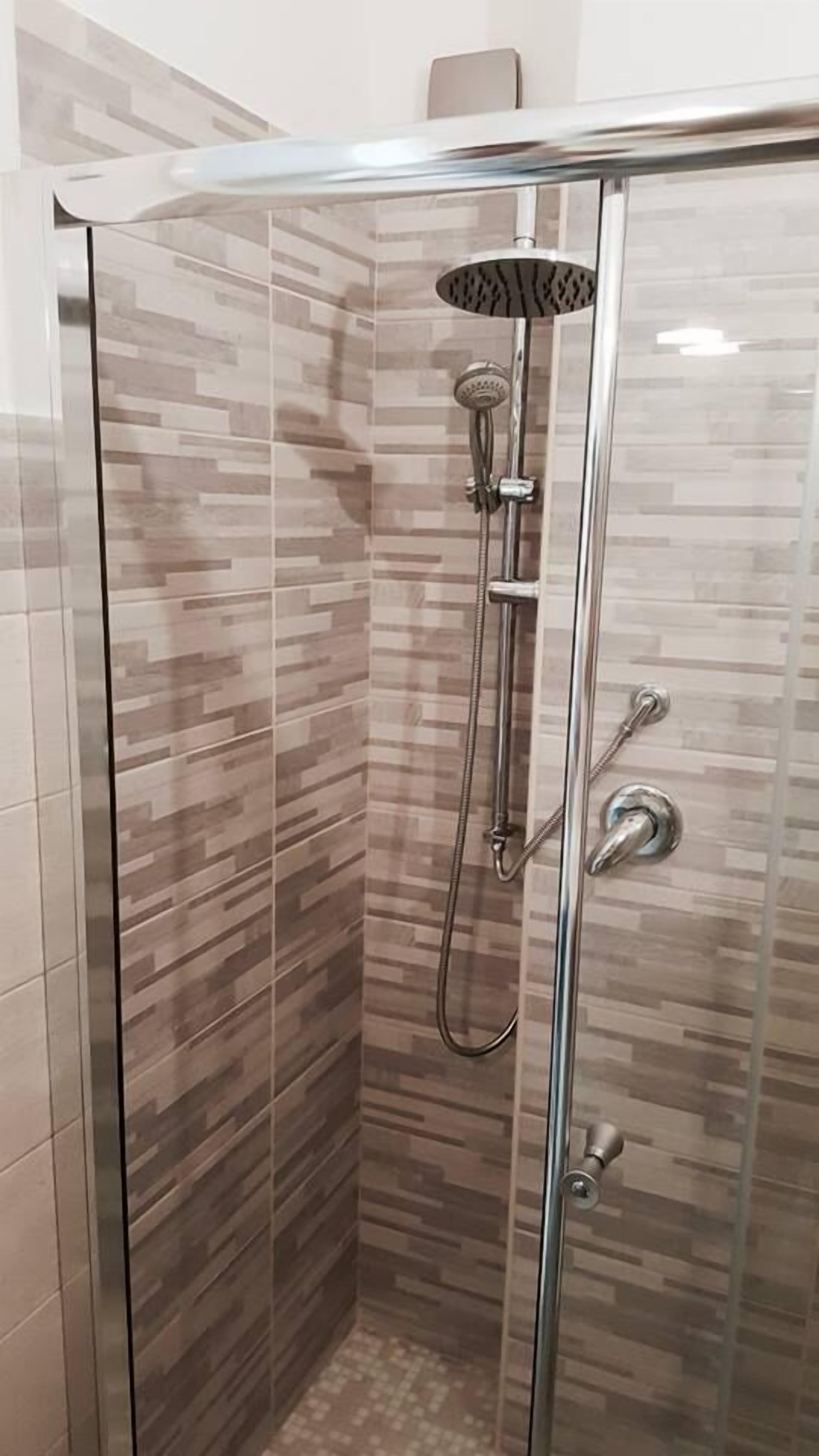 Cabina de ducha con paredes de vidrio, ducha de lluvia, ducha de mano y grifo de mano.