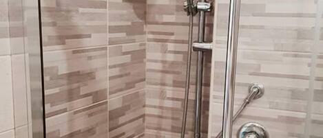 Cabina de ducha con paredes de vidrio, ducha de lluvia, ducha de mano y grifo de mano.
