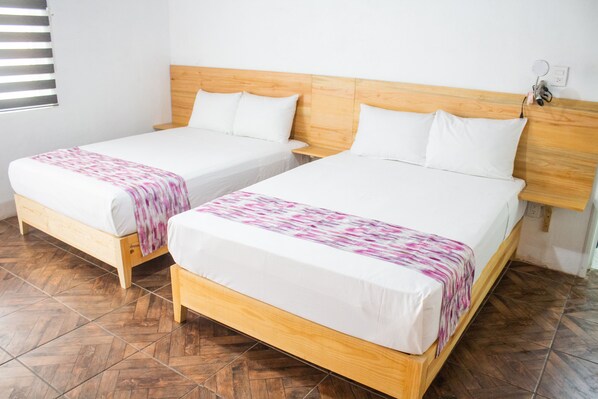 Duas camas de solteiro com cabeceiras de madeira, roupa de cama branca e piso com padrão herringbone.