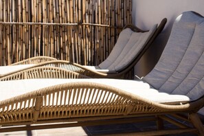 Cadeiras de vime para relaxar com almofadas, colocadas em frente a um muro de bambu.