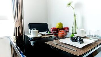 A dining area with a black table, white plates, a fruit basket, and a vase with a single flower.