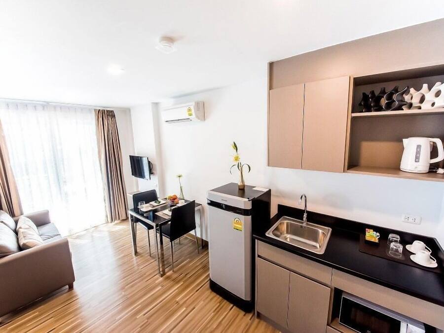 Una habitación de hotel compacta con kitchenette, un sofá, una mesa de comedor y una pequeña encimera de cocina.