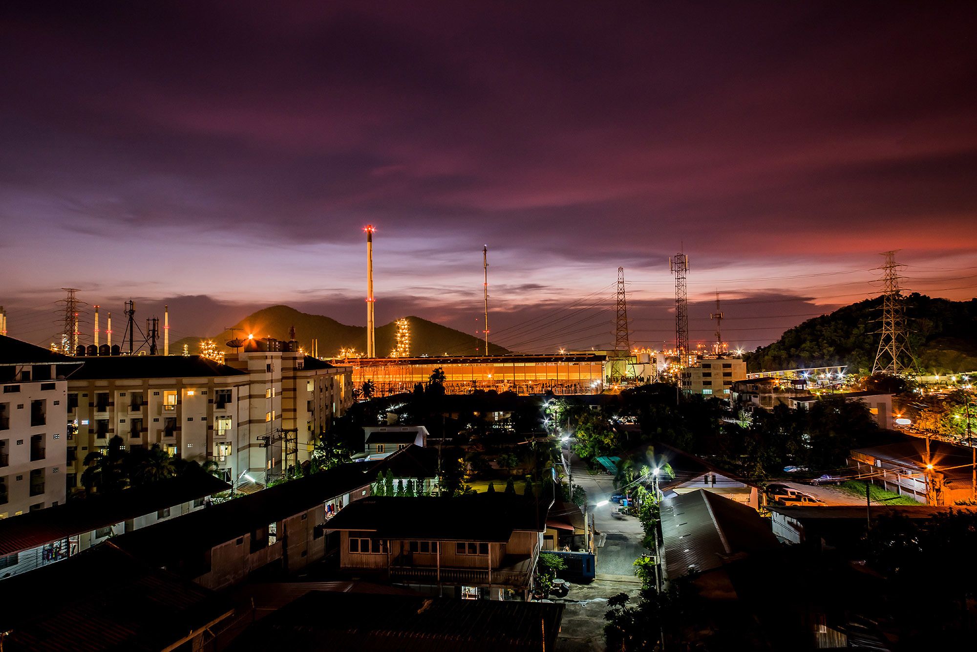 A nighttime view of a cityscape with industrial buildings, a prominent tower, and a bridge.