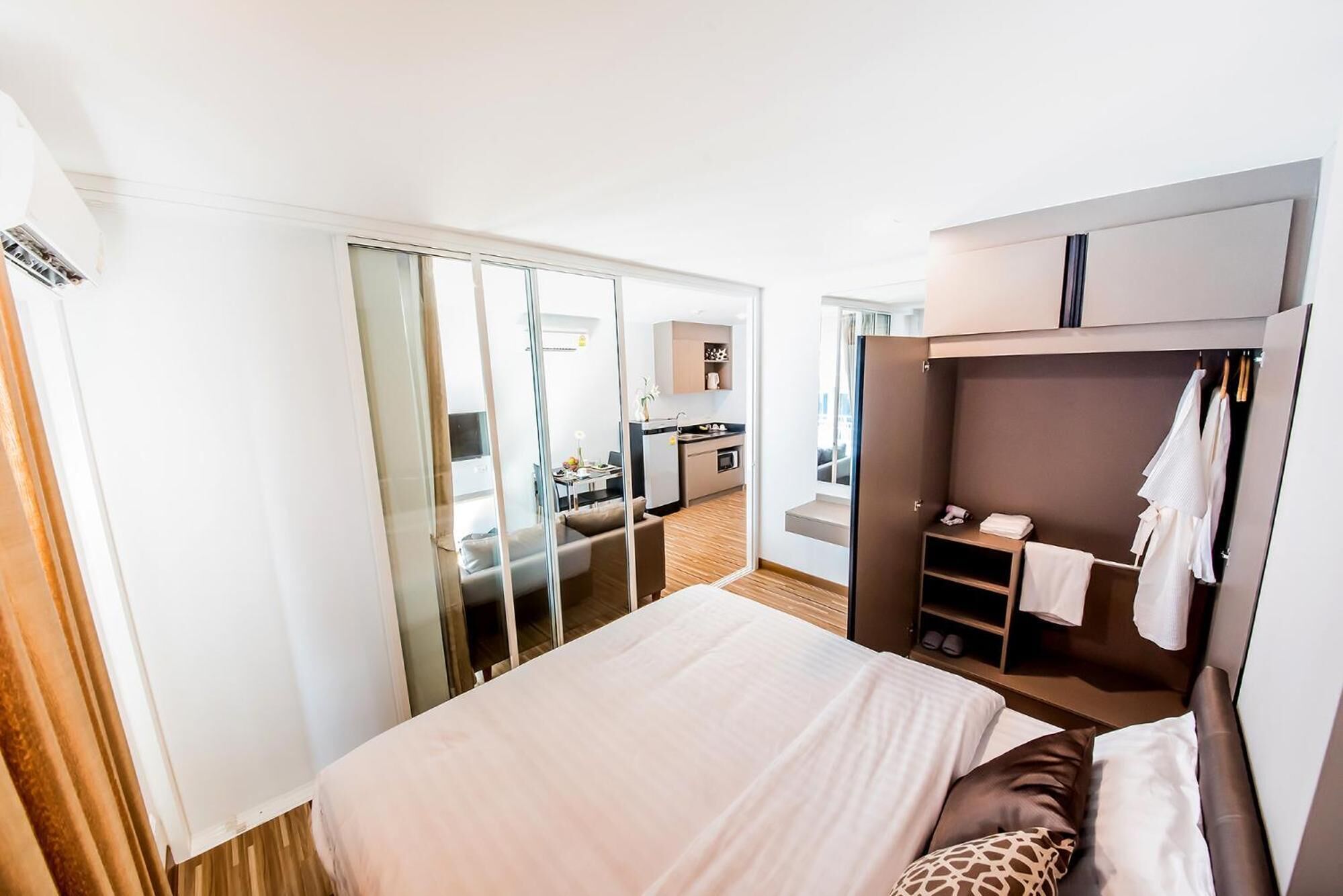 Quarto de hotel com cama, guarda-roupa, uma kitchenette pequena e porta deslizante para uma casa de banho.