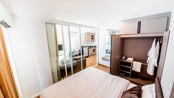 Quarto de hotel com cama, guarda-roupa, uma kitchenette pequena e porta deslizante para uma casa de banho.