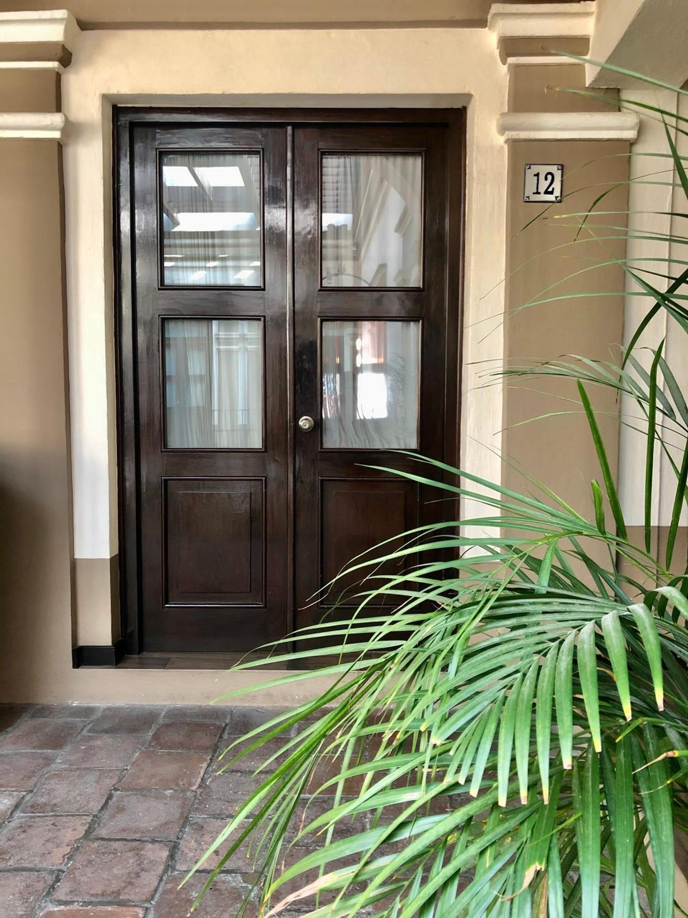 A dark wooden door with glass panels, a number '12' sign, and a potted plant in the foreground.