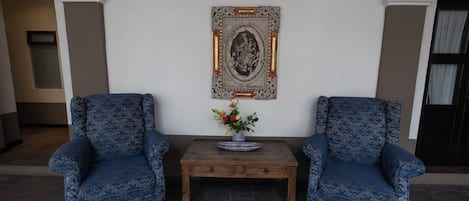 Una habitación con dos sillones azules estampados, una mesa de centro de madera con un jarrón de flores, y un cuadro enmarcado en la pared.