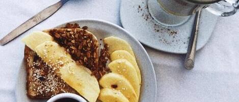 A plate with toast, banana slices, and a small bowl of syrup, alongside a cup of coffee with a frothy top.