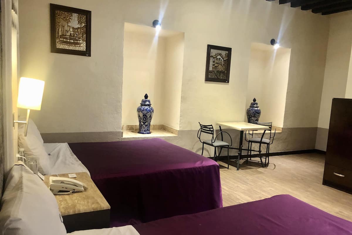 Ein Hotelzimmer mit zwei Betten, einem Schreibtisch, Stühlen, einer Lampe und dekorativen Vasen.