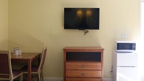 A room with a wooden dining table and chairs, a television mounted on the wall, and a white refrigerator. - Four Corners motel (Montebello)