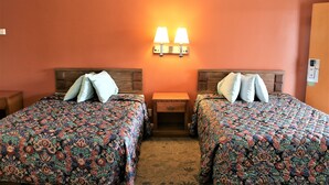 A hotel room with two beds, each with a patterned bedspread, a nightstand, and a wall-mounted lamp between the beds. - Four Corners motel (Montebello)