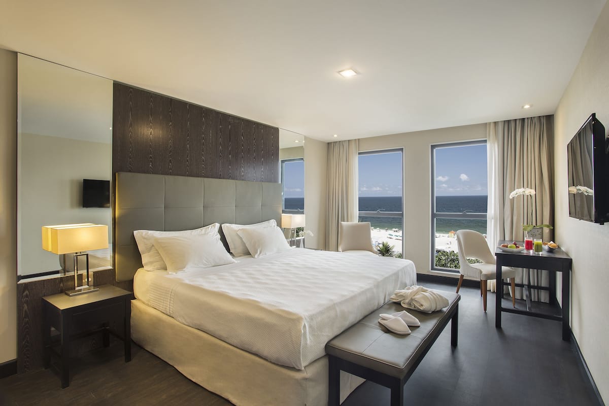A hotel room with a large bed, a desk, a chair, a TV, and a view of the ocean.