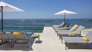 Un espace de détente aménagé au bord de la piscine, avec des chaises longues, des parasols et une vue sur l’océan.