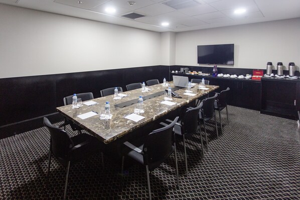A conference room with a long table, chairs, water bottles, a laptop, and a coffee station.
