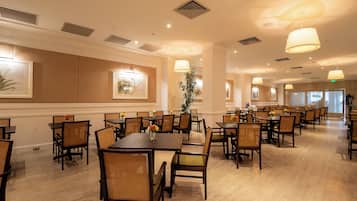 A spacious dining area with multiple tables and chairs, ceiling lights, and framed artwork on the walls.