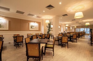 A spacious dining area with multiple tables and chairs, ceiling lights, and framed artwork on the walls.