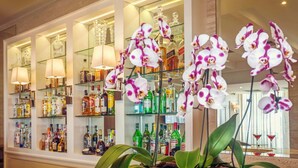 Un espace bar avec des étagères remplies de bouteilles d’alcool, un miroir et des orchidées.