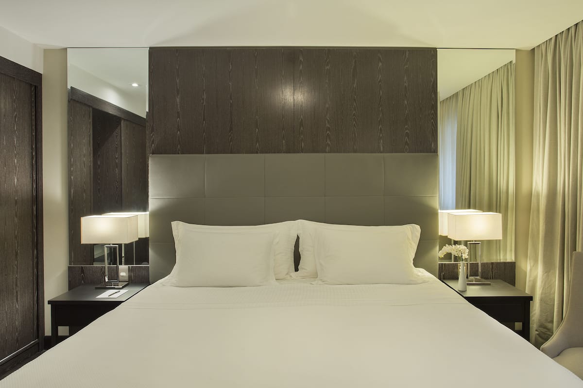 Een moderne hotelkamer met een groot bed, twee nachtkastjes met lampen en een grote spiegel.