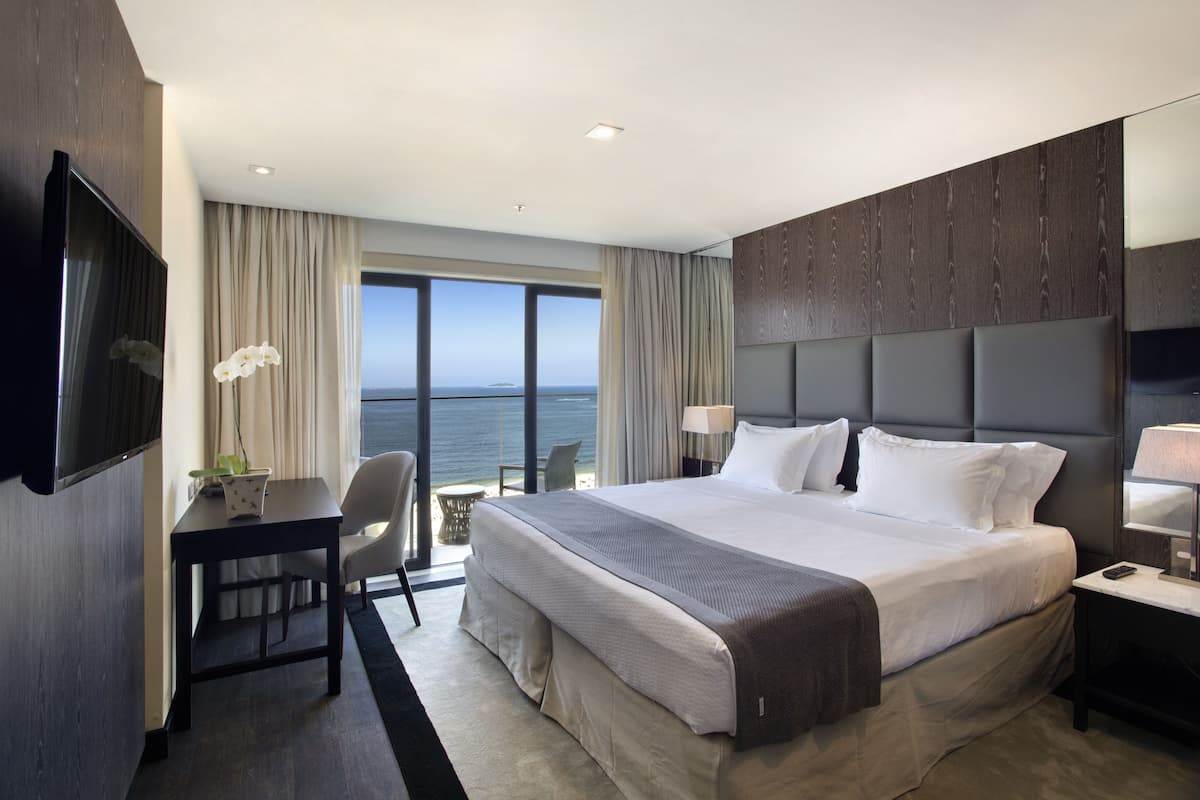 Hotelkamer met een groot bed, een bureau, een stoel, een televisie en uitzicht op zee.