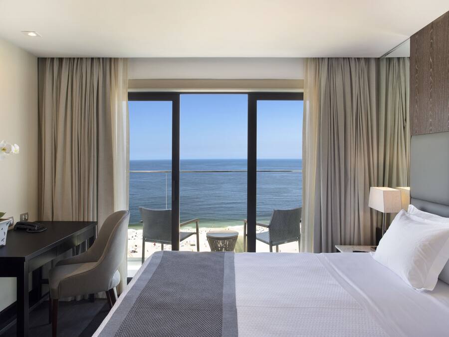 A hotel room with a large bed, a desk, a chair, and a view of the ocean.