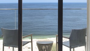 Een balkon met twee stoelen en een kleine tafel, met uitzicht op een strand met mensen en een rustige zee.