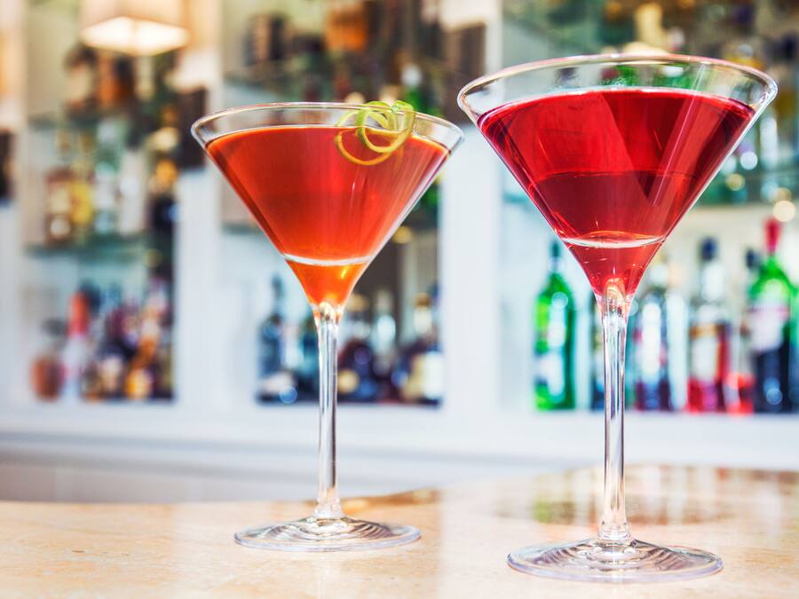 Two martini glasses with red cocktails on a bar counter.