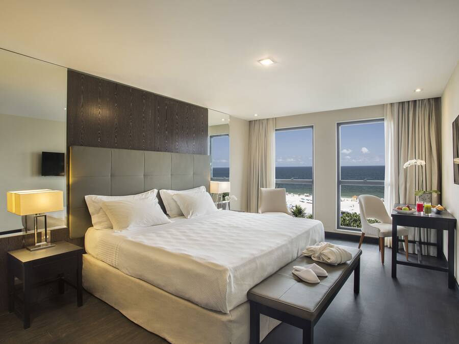 Ein modernes Hotelzimmer mit einem großen Bett, Nachttischen, einem Schreibtisch und Meerblick.
