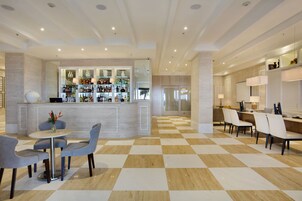 A modern hotel lobby with a checkered floor, a bar area with a variety of bottles, and seating arrangements.