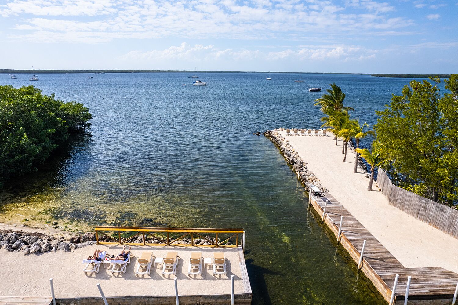 A beach with clear water, a dock, and lounge chairs.