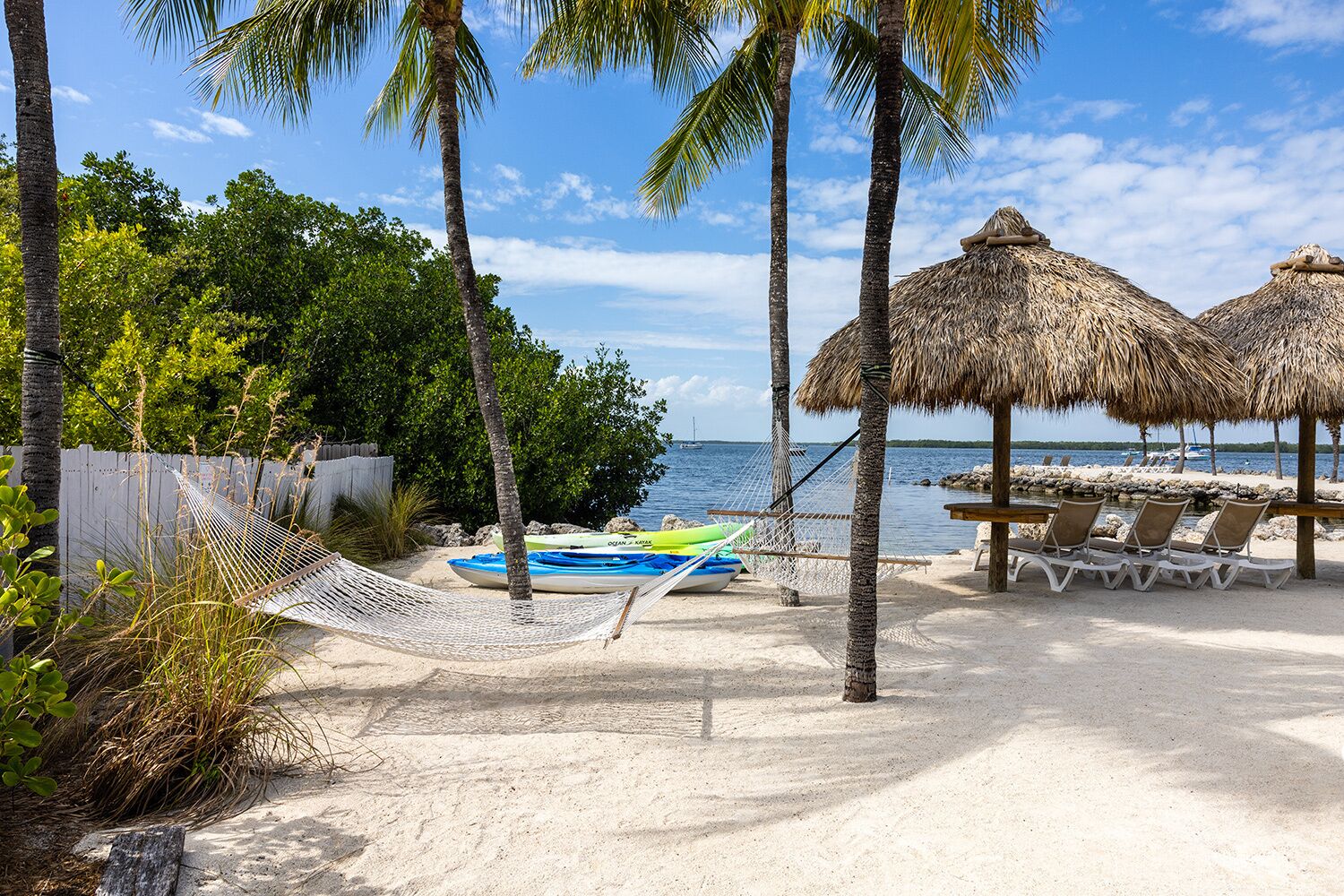 A beach with a hammock, lounge chairs, and thatched umbrellas.
