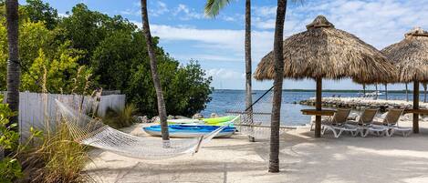 A beach with a hammock, lounge chairs, and thatched umbrellas.