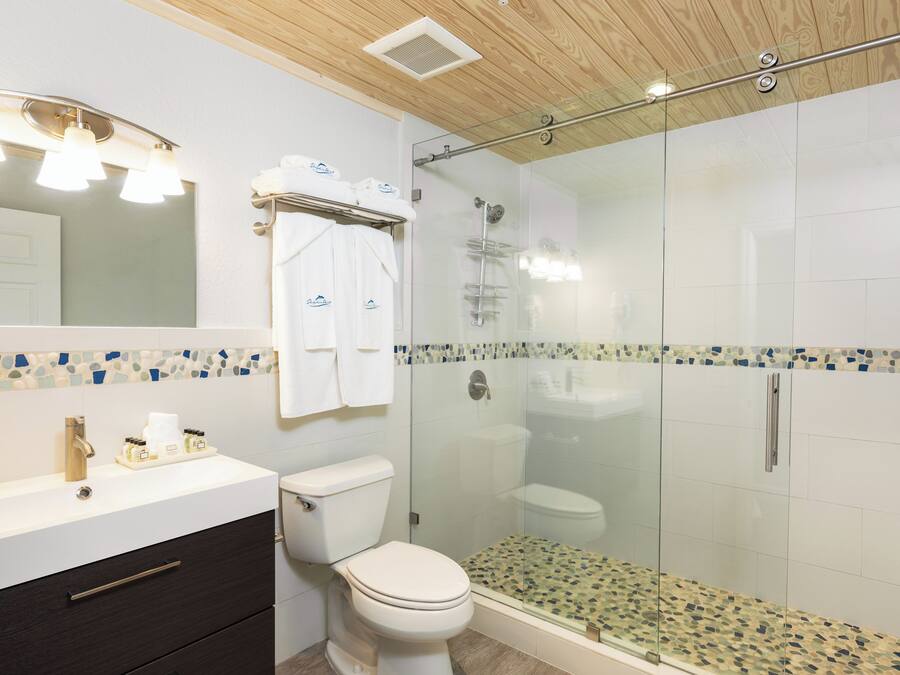 A modern bathroom with a glass-enclosed shower, a white sink with a gold faucet, and a dark wood vanity.