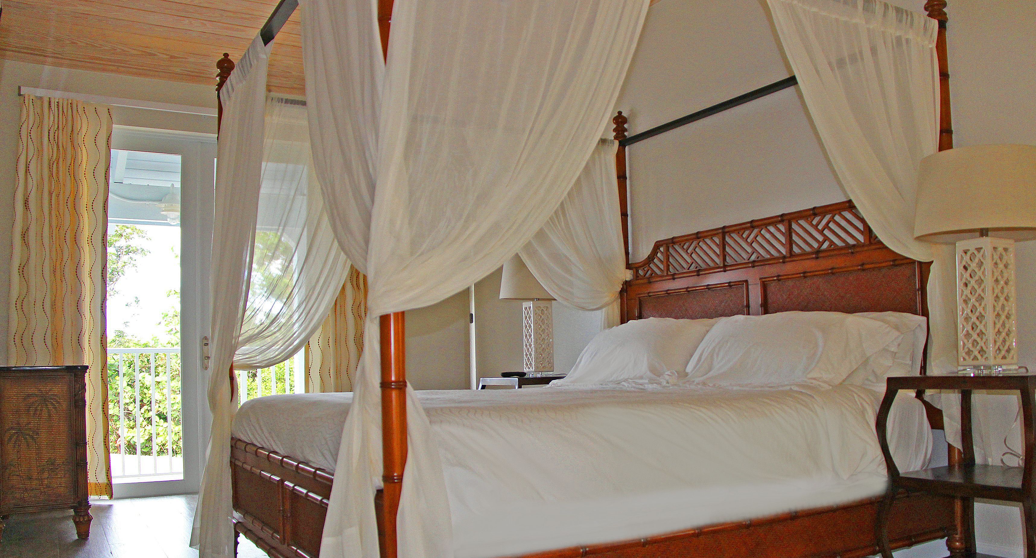 A four-poster canopy bed with white linens, a wooden headboard, and a bedside table with a lamp.