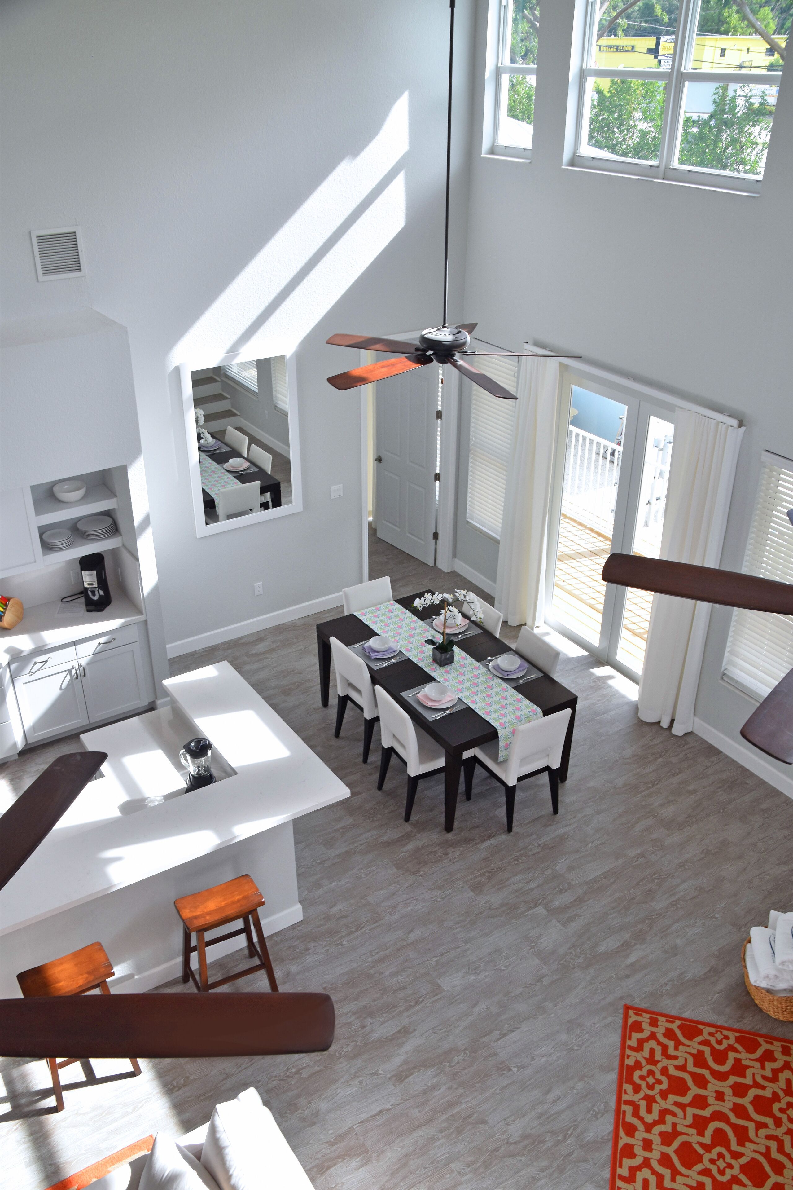 A spacious dining area with a high ceiling fan, a kitchen area with white cabinets, and a large window providing a view of the outside.