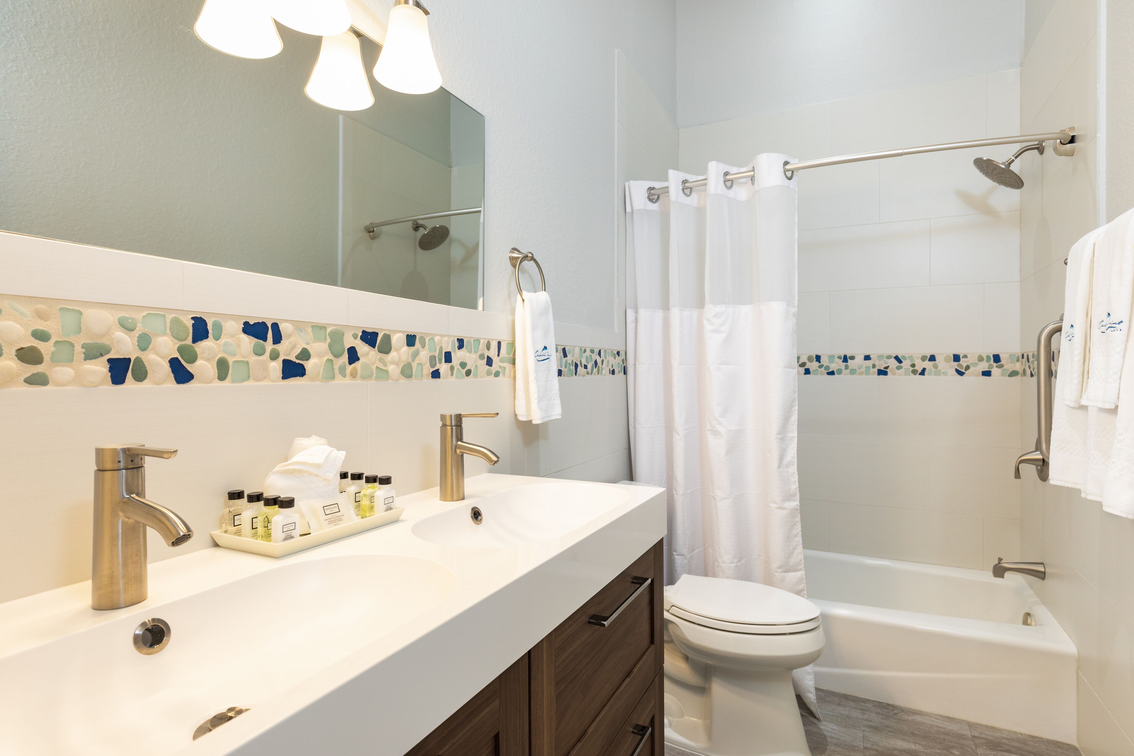 Une salle de bain moderne avec un lavabo blanc, deux robinets, un miroir et un espace douche séparé par un rideau.