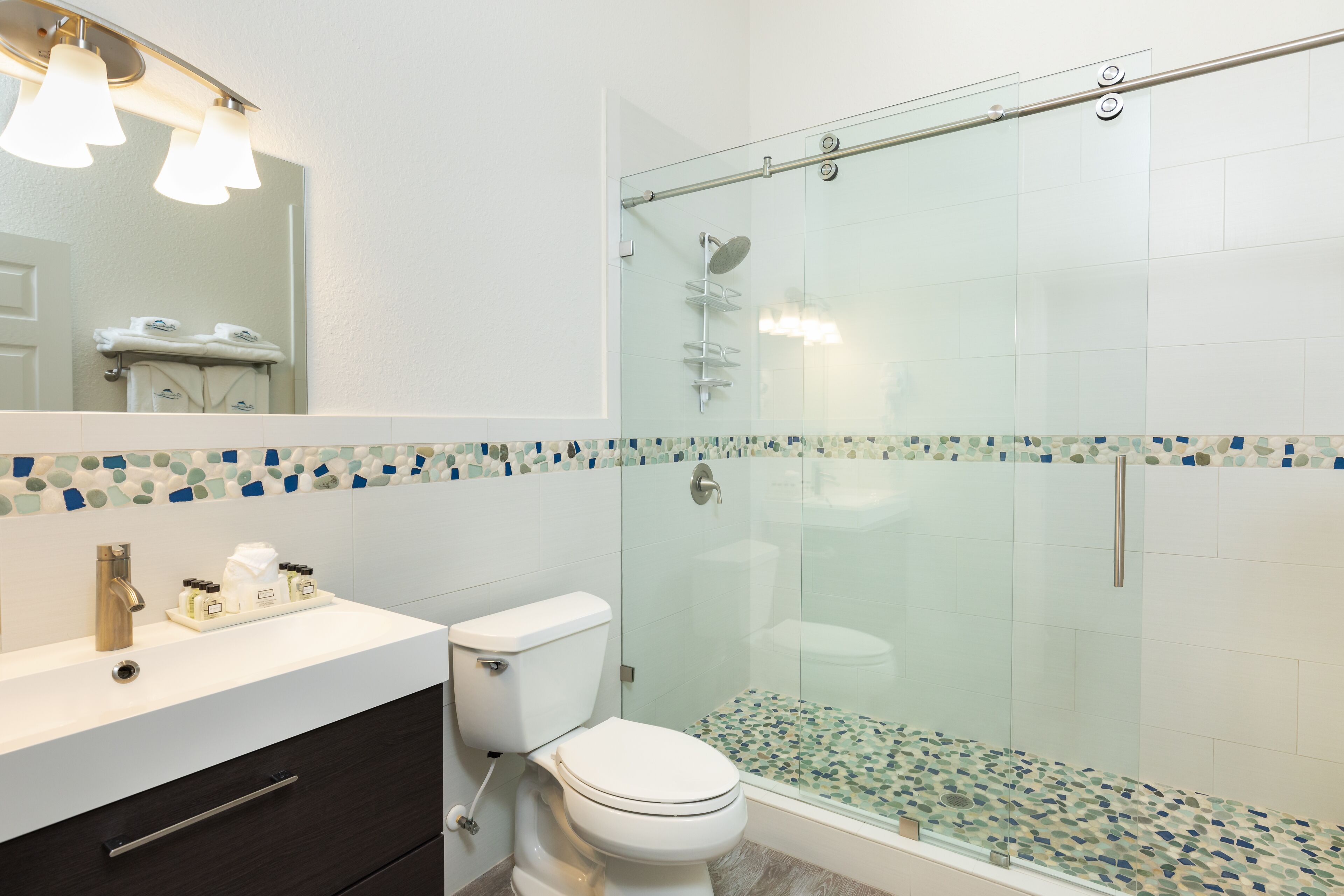 Une salle de bain moderne avec une douche à parois de verre, des toilettes blanches et un meuble-lavabo doté d’un miroir et d’un porte-serviettes.