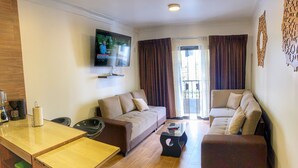 A modern living room with a sofa set, a coffee table, a TV mounted on the wall, and a dining area with a table and chairs. - Del Niño Apartments (Cusco)