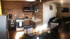 A compact kitchen with a microwave, stove, and coffee maker, a dining area with a glass table, and a living room with a sofa and TV. - Del Niño Apartments (Cusco)